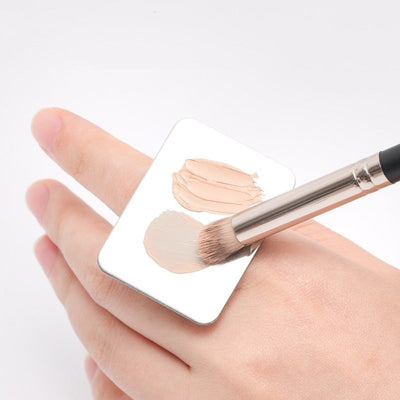 Beauty product foundation palette with color swatches on hand, makeup brush preparing colors for blending.